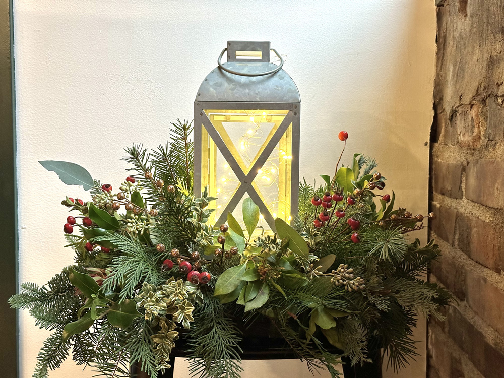 Holiday Lantern arrangements nestled in a collection of winter greens, berries, baubles and ribbons at a floral design class in Snohomish Washington at Fleurs Creative